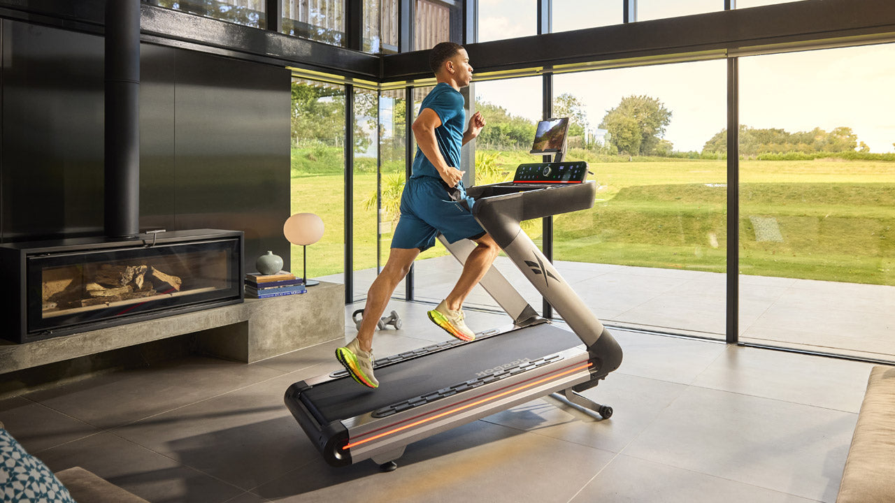 Person using a treadmill in a modern living room with large windows.